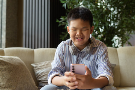 Happy Thai boy using phone at cafe with headphonesの写真素材