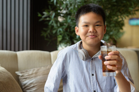 Happy Thai boy drinking soda and smiling at camera in restaurantの写真素材