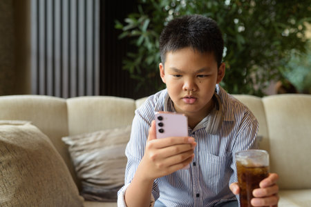 Thai boy drinking soda and using phone at restaurant with headphonesの写真素材