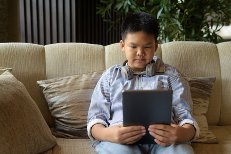 Young Thai boy using digital tablet computer at cafe with headphonesの写真素材
