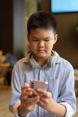 Handsome Thai boy using phone at cafe with headphonesの写真素材