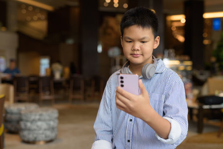 Handsome Thai boy using phone at cafe with headphonesの写真素材