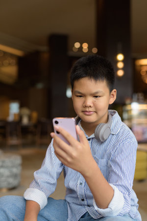Handsome Thai boy using phone at cafe with headphonesの写真素材