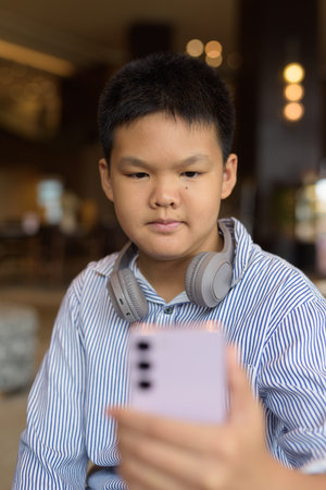 Handsome Thai boy using phone at cafe with headphonesの写真素材
