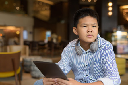 Thai boy using digital tablet computer at cafe with headphones aloneの写真素材