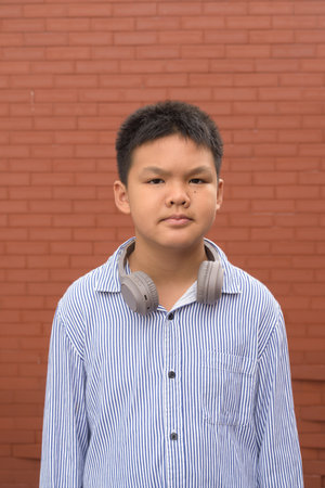 Thai boy in formal shirt with headphones posing against brick wall outdoorsの写真素材