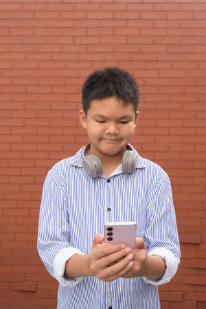 Thai boy in formal shirt with headphones posing against brick wall outdoorsの写真素材