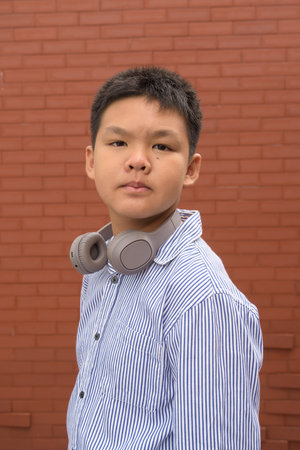 Thai boy in formal shirt with headphones posing against brick wall outdoorsの写真素材