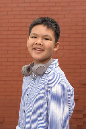 Thai boy in formal shirt with headphones posing against brick wall outdoorsの写真素材