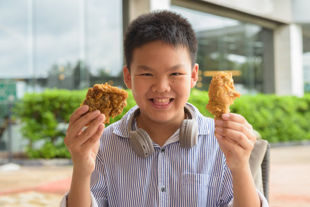 Thai student boy eating fried chicken with headphones at outdoor tableの写真素材