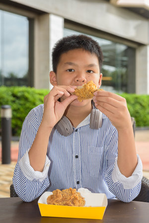Thai student boy eating fried chicken with headphones at outdoor tableの写真素材