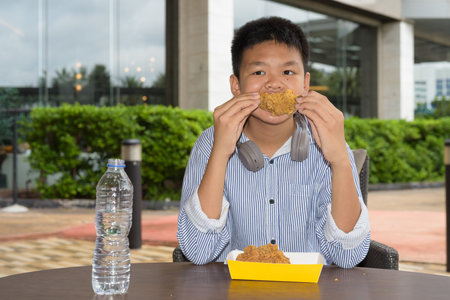 Thai student boy eating fried chicken and drinking water outdoorsの写真素材