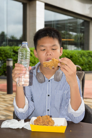 Thai student boy eating fried chicken and drinking water outdoorsの写真素材