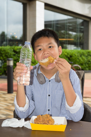 Thai student boy eating fried chicken and drinking water outdoorsの写真素材