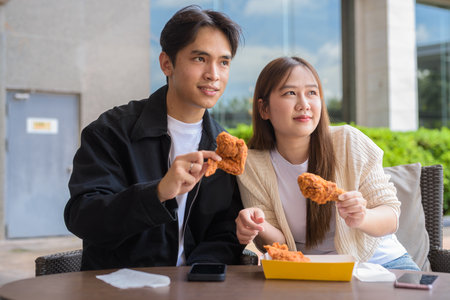 Young Asian couple eating fried chicken outdoorsの写真素材