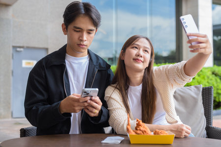 Young Asian couple eating fried chicken outdoorsの写真素材