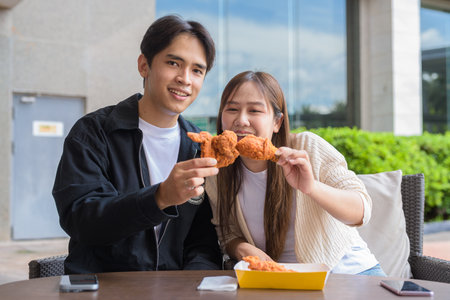 Young Asian couple eating fried chicken outdoorsの写真素材