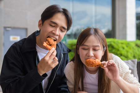 Young Asian couple eating fried chicken outdoorsの写真素材