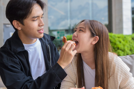 Young Asian couple eating fried chicken outdoorsの写真素材
