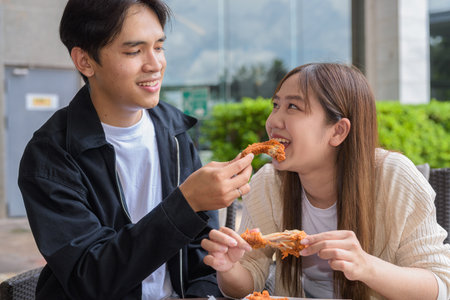 Young Asian couple eating fried chicken outdoorsの写真素材