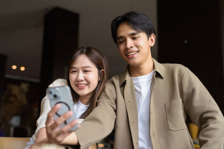 Portrait of a happy young Asian couple taking selfie in cafe with smartphoneの写真素材