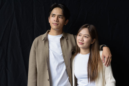 Studio portrait of young couple against dark background thinking and looking awayの写真素材