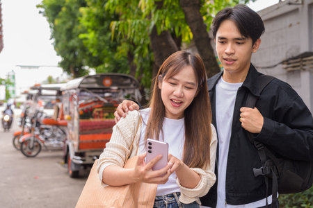 Young Asian tourist couple ordering taxi with mobile app while on street togetherの写真素材
