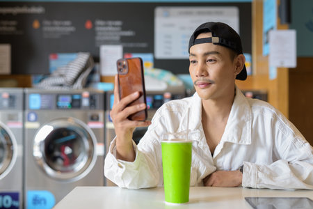 Portrait of non binary gay man sitting in laundry shopの写真素材