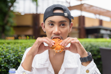 Portrait of non binary gay man eating fried chicken and drinking cola outdoors during summerの写真素材