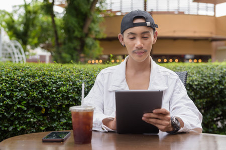 Cute non binary gay man drinking coffee in outdoors cafe restaurant during summer