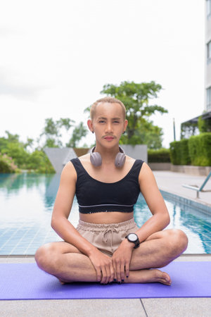 Non-binary Asian person exercising in poolside doing yoga and wearing sport bra
