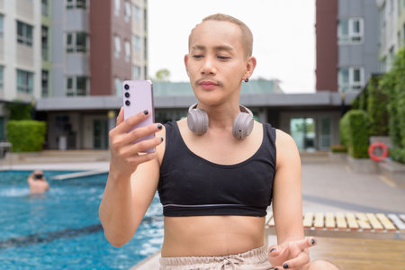 Non-binary Asian person relaxing in poolside during summer wearing sport braの写真素材