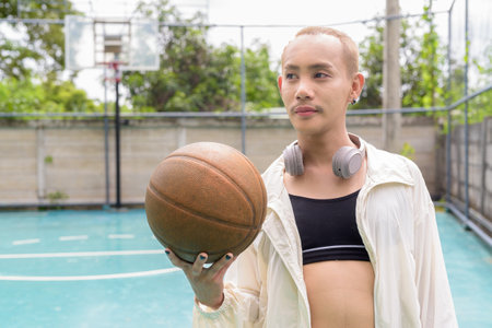 Queer non-binary Asian model holding basketball outdoors