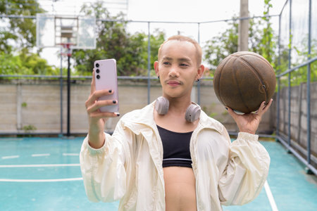 Queer non-binary Asian model holding basketball outdoors