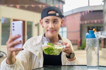 Nonbinary Asian person eating healthy caesar salad outdoorsの写真素材