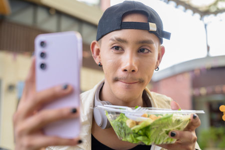 Nonbinary Asian person eating healthy caesar salad outdoorsの写真素材