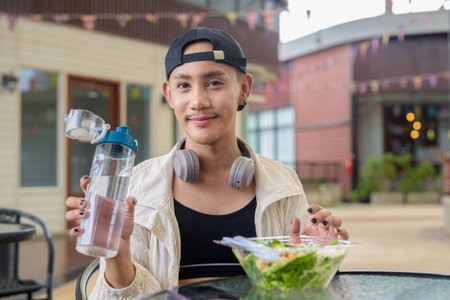 Nonbinary Asian person eating healthy caesar salad outdoorsの写真素材