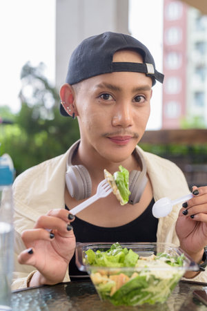 Nonbinary Asian person eating healthy caesar salad outdoorsの写真素材