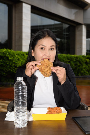 Asian mature woman eating fried chicken in outdoors restaurant