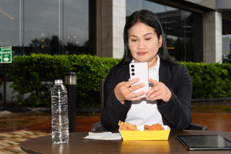 Asian mature woman eating fried chicken in outdoors restaurantの写真素材