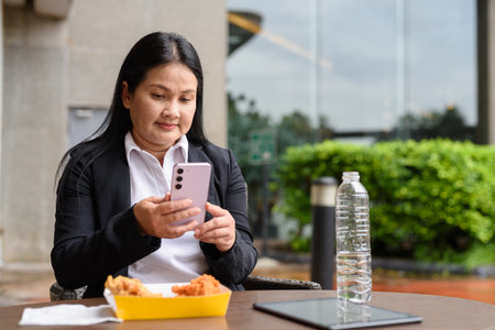 Asian mature woman eating fried chicken in outdoors restaurantの写真素材