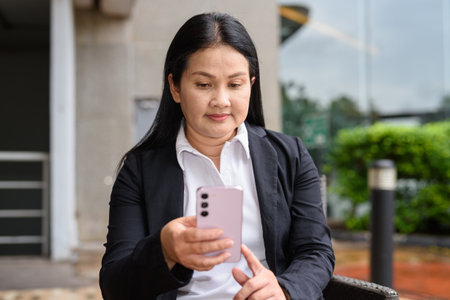 Woman using mobile phone outdoors while sittingの写真素材