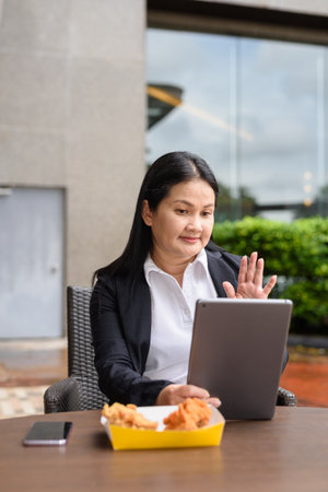 Asian mature woman eating fried chicken in outdoors restaurantの写真素材