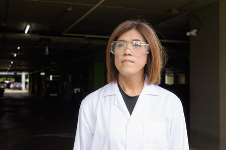 Confident transgender STEM profession non-binary person in lab coat and protective glassesの写真素材