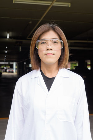 Confident transgender STEM profession non-binary person in lab coat and protective glassesの写真素材
