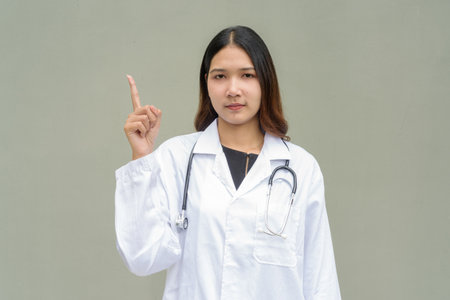 Young Asian woman doctor wearing white lab coat and stethoscope against plain backgroundの写真素材