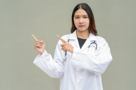 Young Asian woman doctor wearing white lab coat and stethoscope against plain backgroundの写真素材