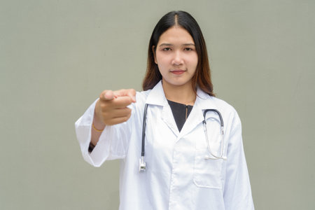Young Asian woman doctor wearing white lab coat and stethoscope against plain backgroundの写真素材
