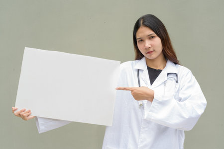 Young Asian woman doctor wearing white lab coat and stethoscope against plain backgroundの写真素材