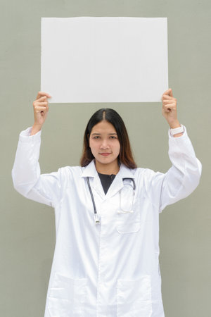 Young Asian woman doctor wearing white lab coat and stethoscope against plain backgroundの写真素材